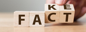 Wooden blocks used to spell fake and fact using different spellings on faces of the blocks